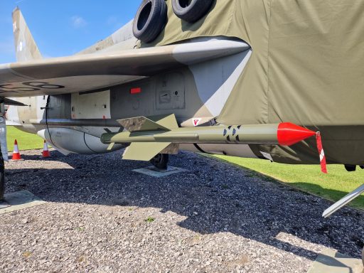 Side view of a military aircraft with a missile mounted underneath its wing.