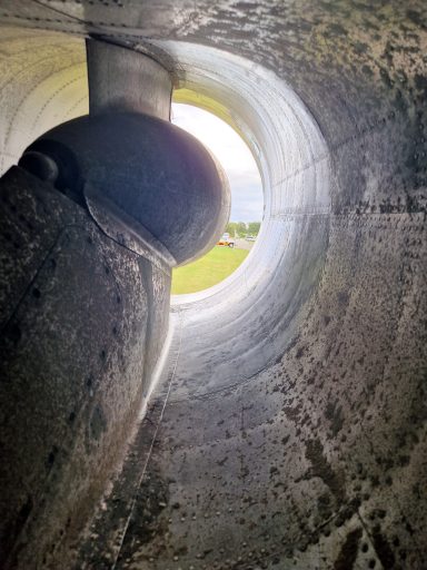 View through a large concrete pipe, showing green fields beyond.