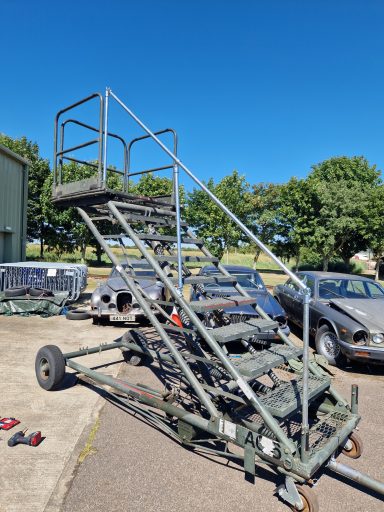 Military-style metal staircase on wheels, set against a clear blue sky.
