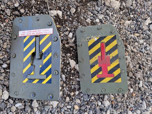 Two metal signs on a gravel surface, featuring yellow and black stripes with symbols.