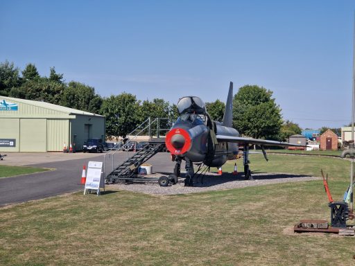 A military aircraft on display outside a hangar, with a clear blue sky.