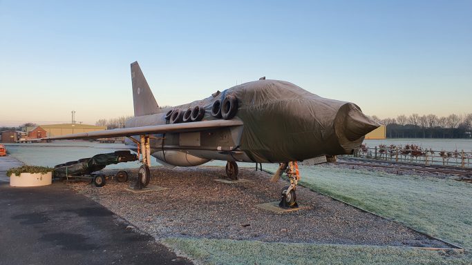 A grey aircraft displayed outdoors on a frosty morning.