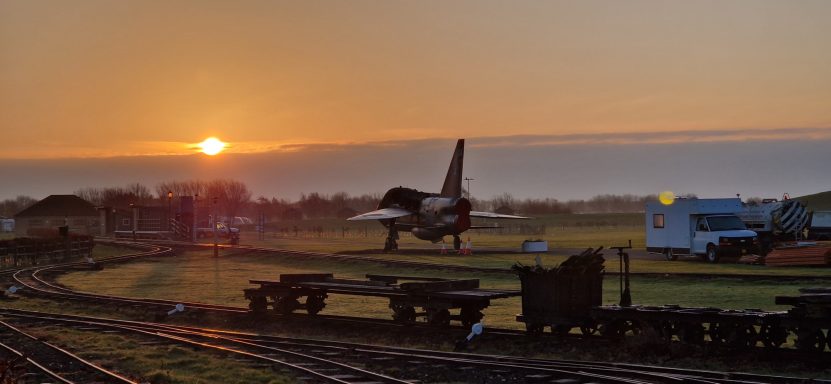 Sunset over a landscape featuring a plane and railway tracks.